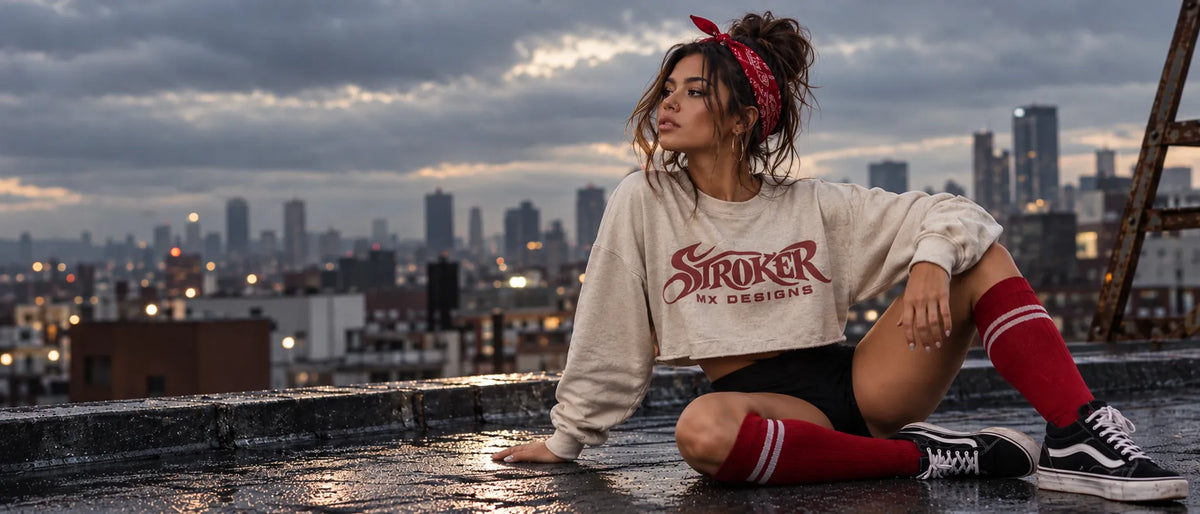 Stroker MX model wearing a cream cropped sweatshirt with burgundy Stroker MX Designs artwork on a city rooftop at dusk